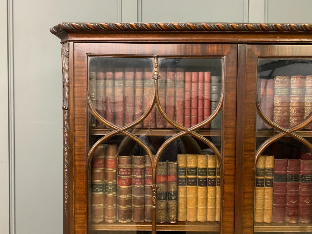 A tall mahogany Chippendale style glazed bookcase featuring three astragal glazed upper doors above three carved panelled lower cupboard doors resting on ball and claw feet. View XVIII
