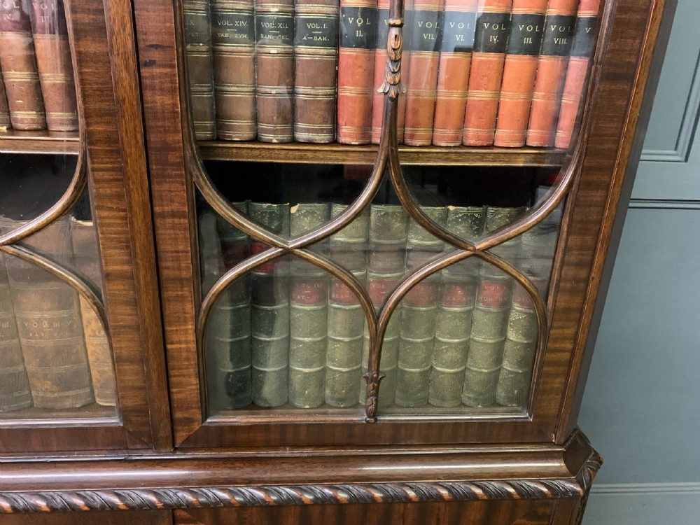 A tall mahogany Chippendale style glazed bookcase featuring three astragal glazed upper doors above three carved panelled lower cupboard doors resting on ball and claw feet. View XX