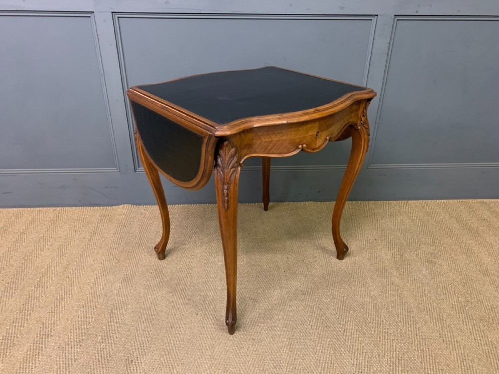 A French walnut drop-leaf table featuring cabriole legs with carved knee foliage and a black inset leather top surface.