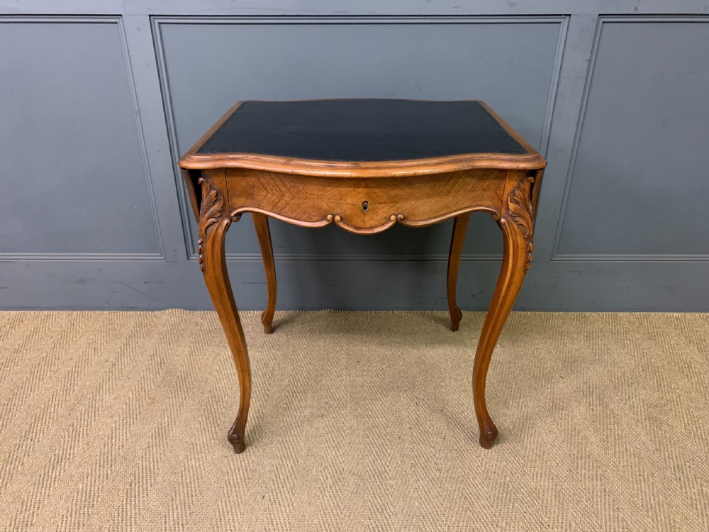 A French walnut drop-leaf table featuring cabriole legs with carved knee foliage and a black inset leather top surface. View II