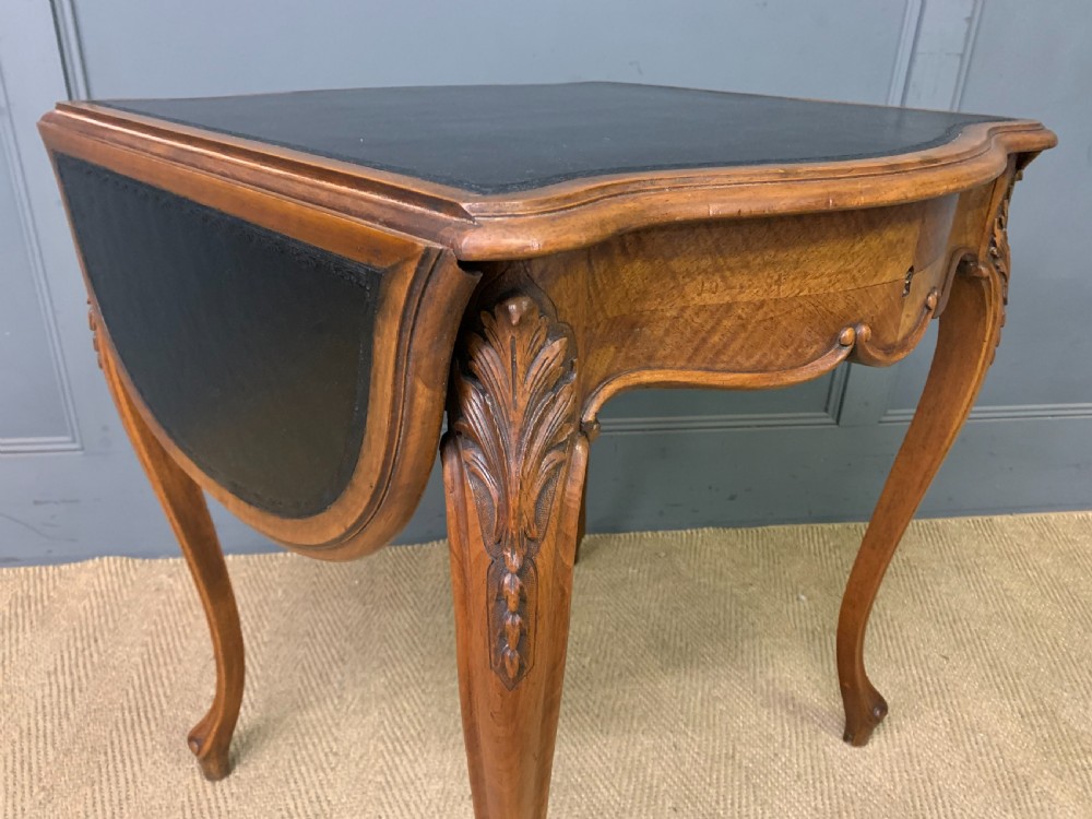 A French walnut drop-leaf table featuring cabriole legs with carved knee foliage and a black inset leather top surface. View VII