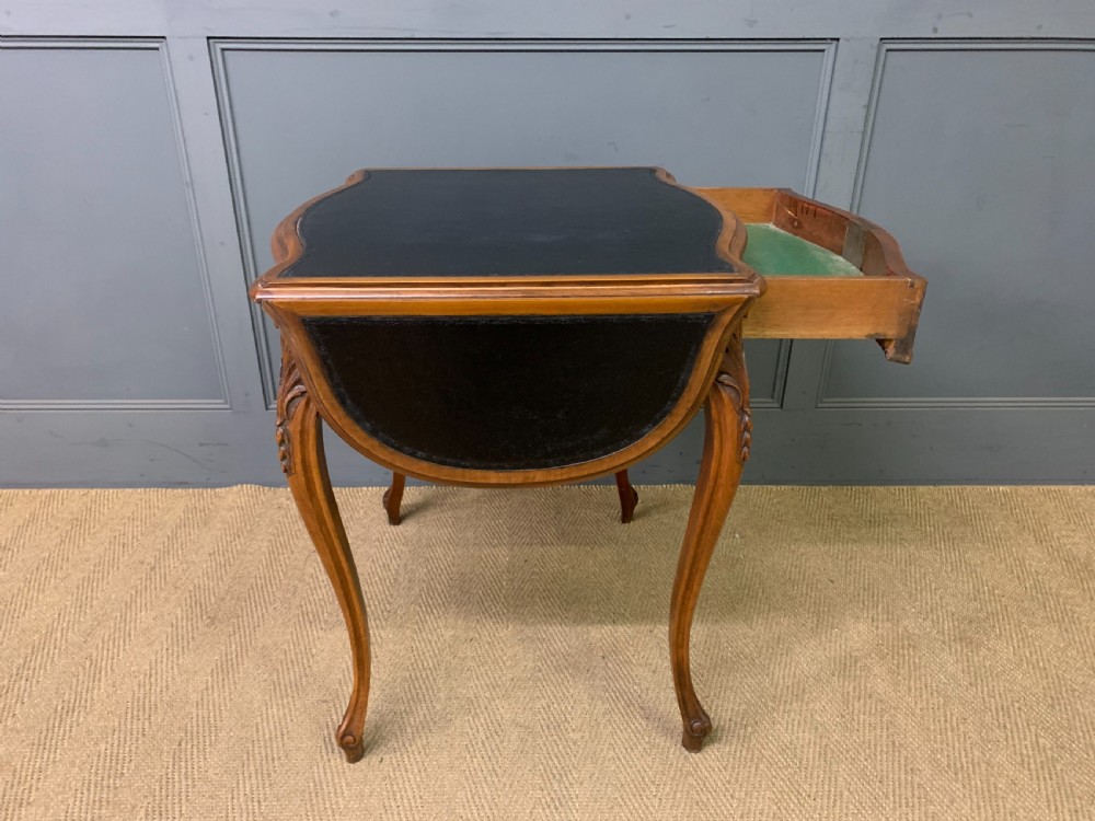 A French walnut drop-leaf table featuring cabriole legs with carved knee foliage and a black inset leather top surface. View IX