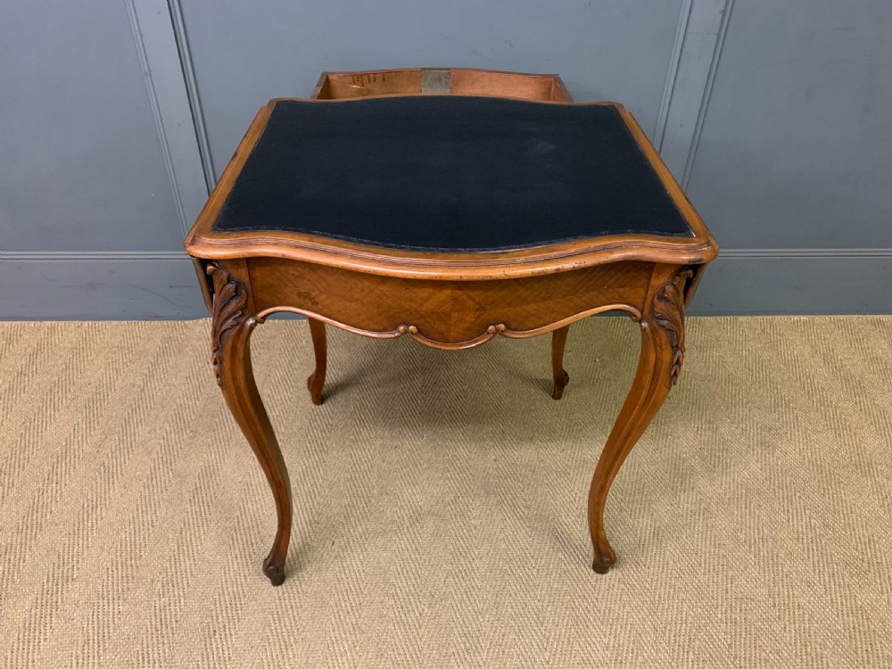 A French walnut drop-leaf table featuring cabriole legs with carved knee foliage and a black inset leather top surface. View X