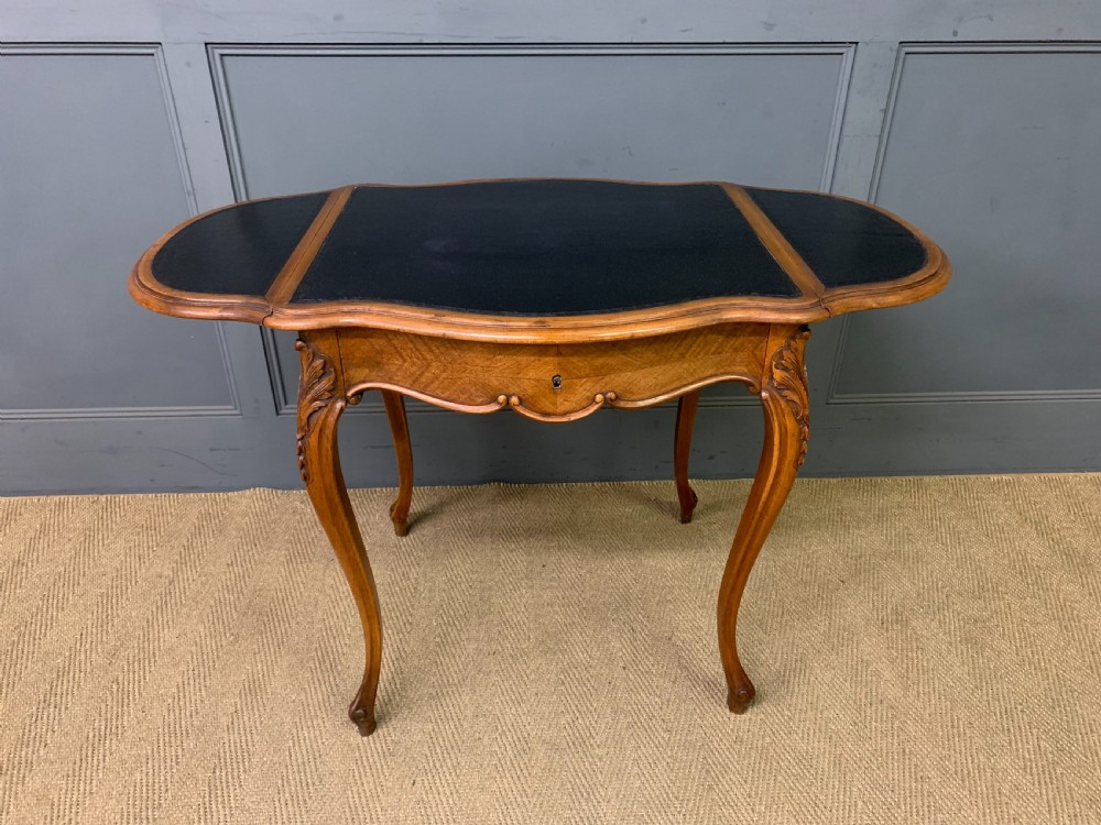 A French walnut drop-leaf table featuring cabriole legs with carved knee foliage and a black inset leather top surface. View XI