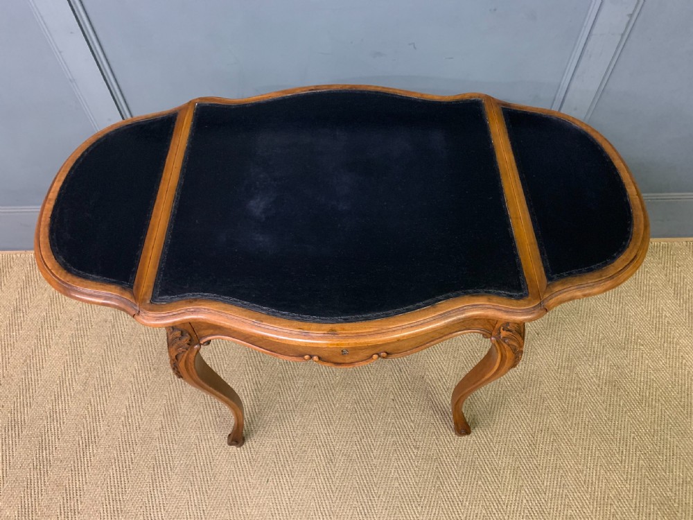 A French walnut drop-leaf table featuring cabriole legs with carved knee foliage and a black inset leather top surface. View XII