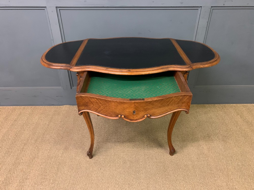 A French walnut drop-leaf table featuring cabriole legs with carved knee foliage and a black inset leather top surface. View XIII