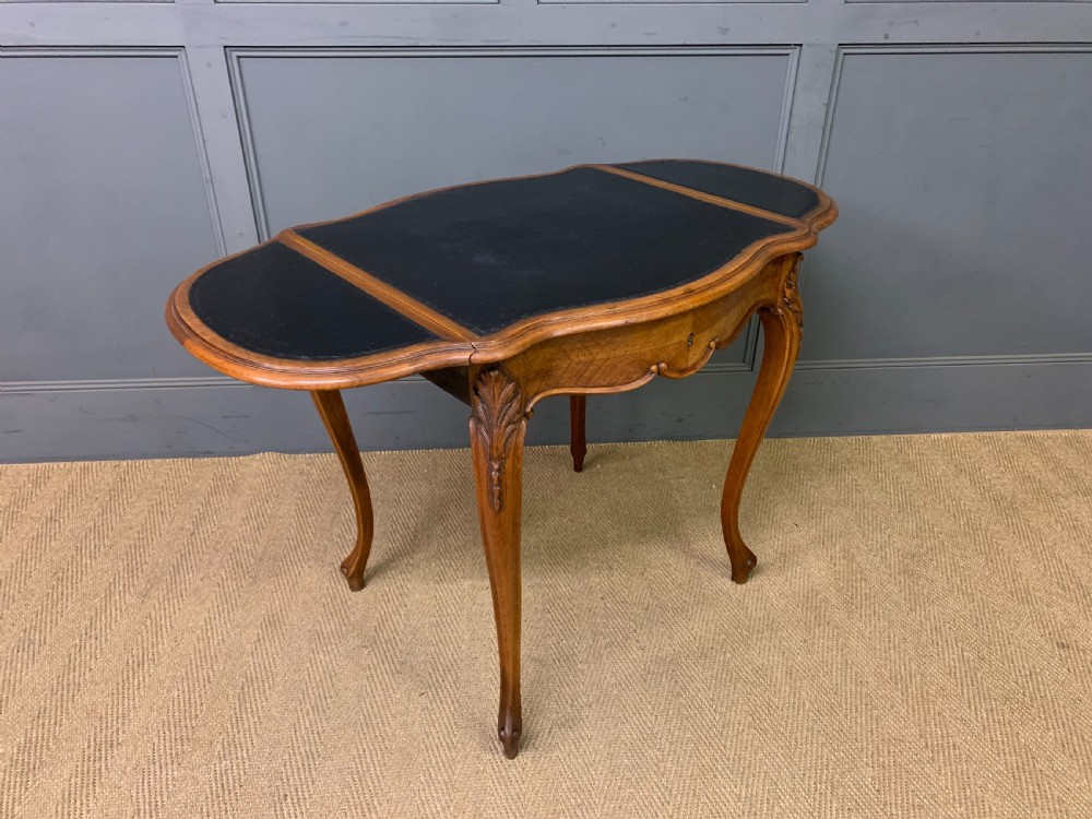 A French walnut drop-leaf table featuring cabriole legs with carved knee foliage and a black inset leather top surface. View XIV