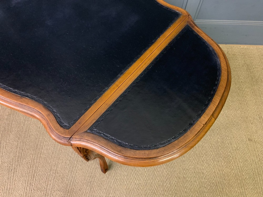 A French walnut drop-leaf table featuring cabriole legs with carved knee foliage and a black inset leather top surface. View XV