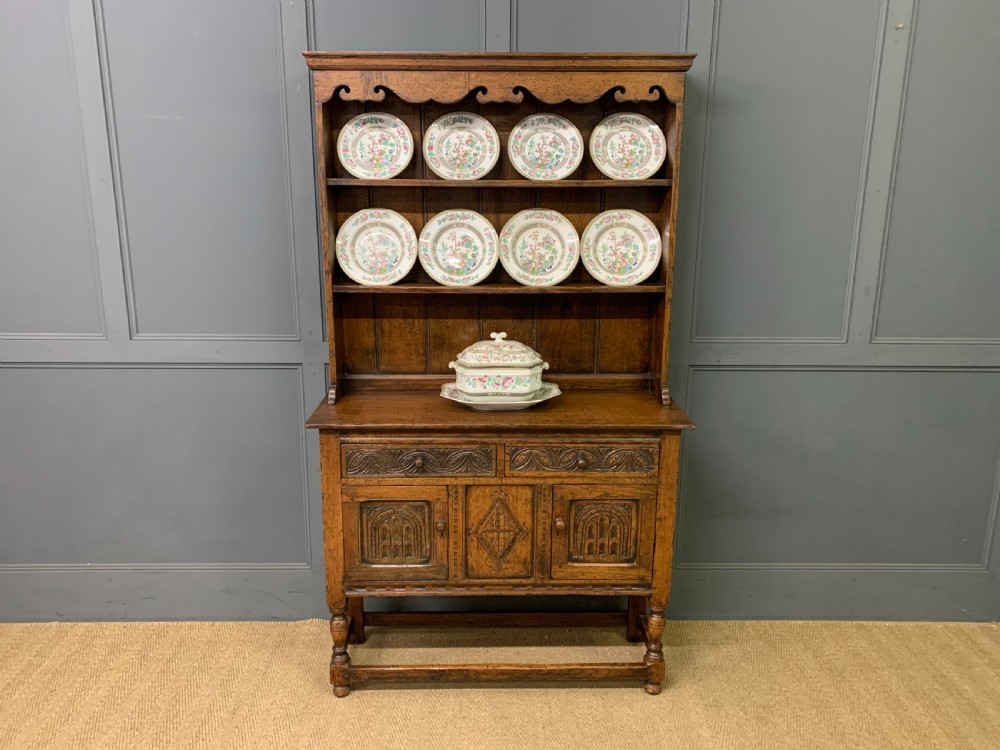 A carved oak Welsh dresser featuring an upper open shelving rack above two carved drawers and panelled cupboard doors resting on turned legs. View II