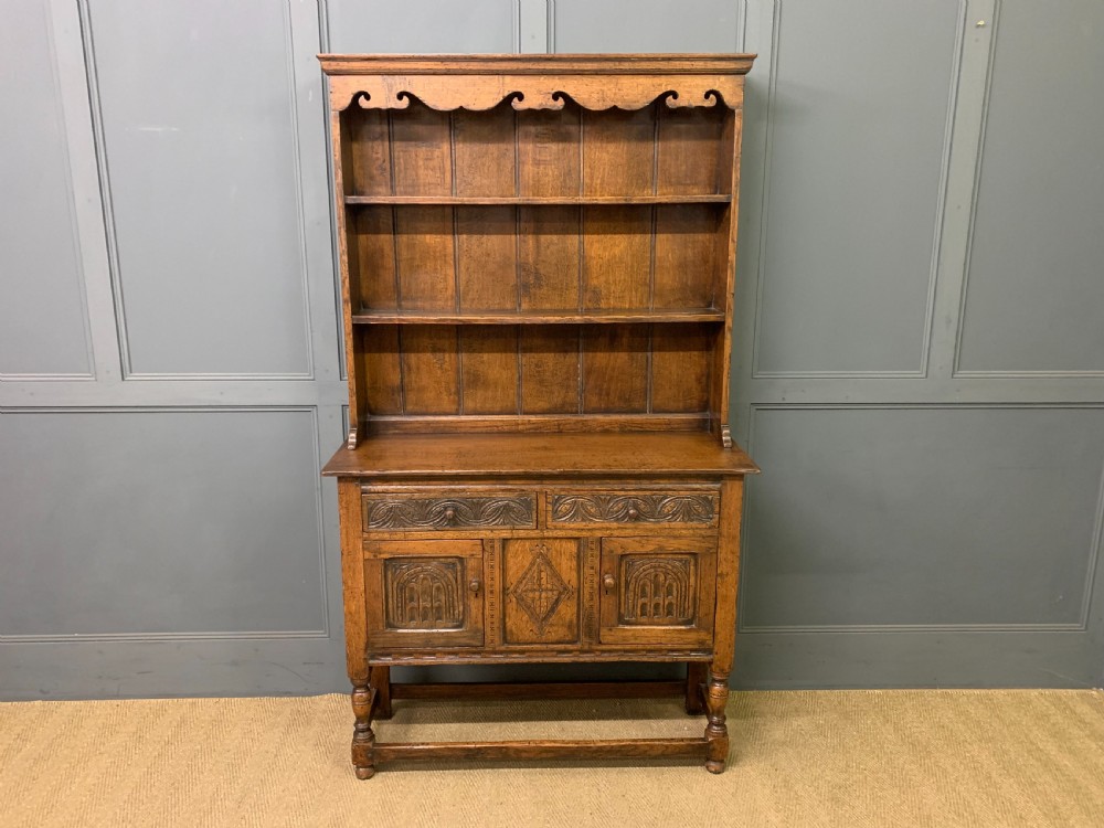 A carved oak Welsh dresser featuring an upper open shelving rack above two carved drawers and panelled cupboard doors resting on turned legs.