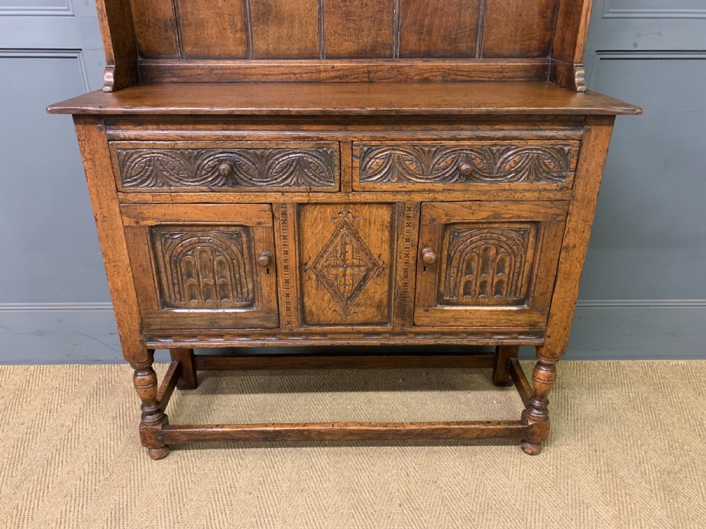 A carved oak Welsh dresser featuring an upper open shelving rack above two carved drawers and panelled cupboard doors resting on turned legs. View III