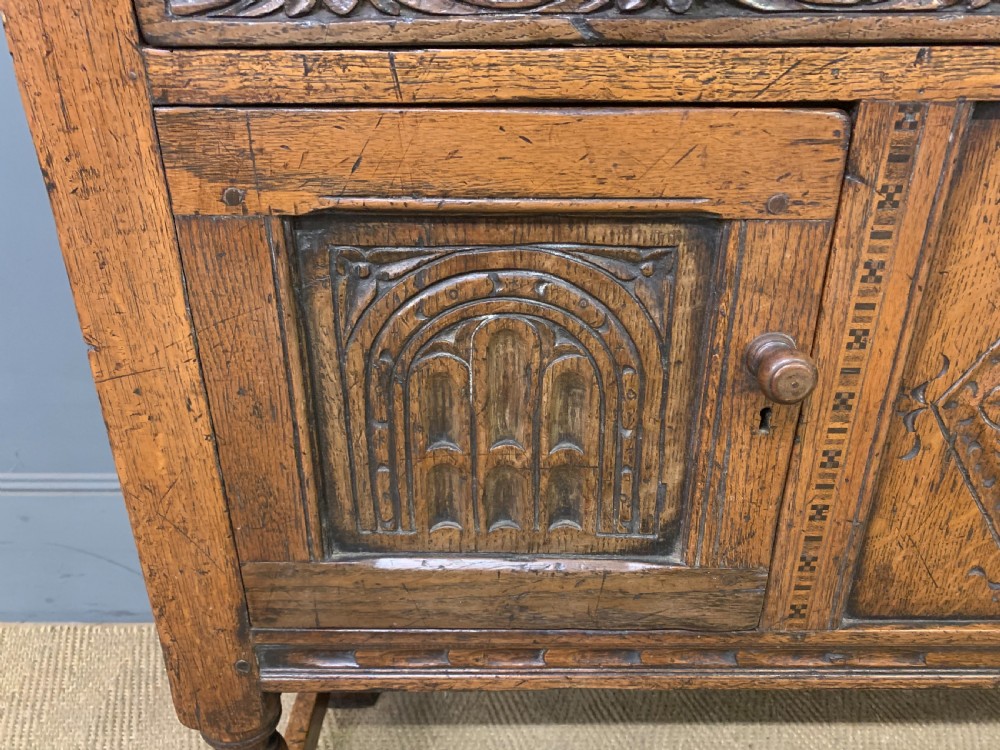 A carved oak Welsh dresser featuring an upper open shelving rack above two carved drawers and panelled cupboard doors resting on turned legs. View V
