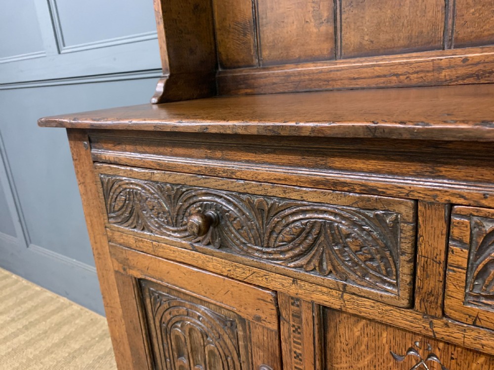A carved oak Welsh dresser featuring an upper open shelving rack above two carved drawers and panelled cupboard doors resting on turned legs. View VI
