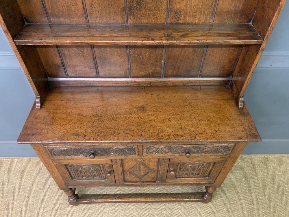 A carved oak Welsh dresser featuring an upper open shelving rack above two carved drawers and panelled cupboard doors resting on turned legs. View VIII