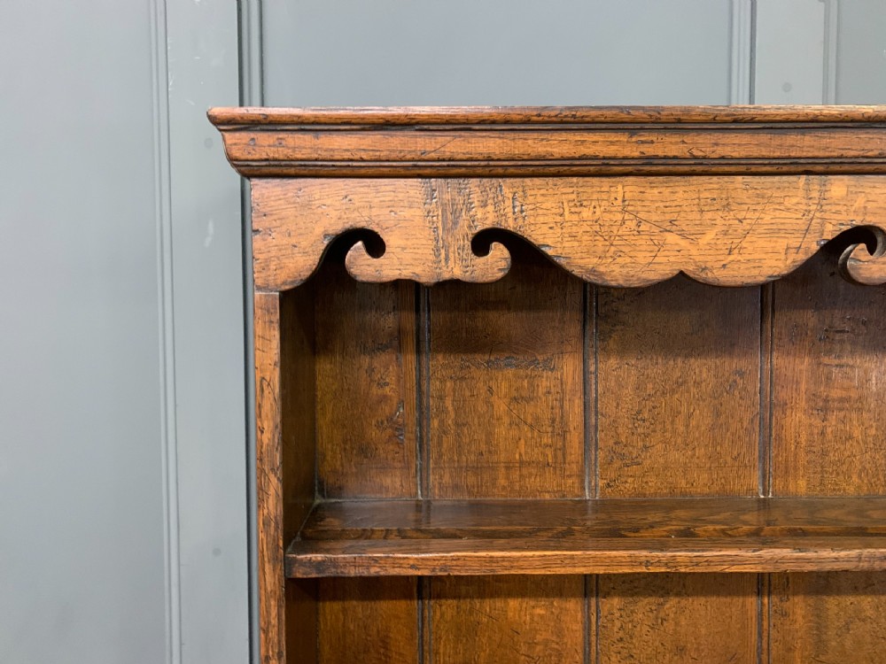 A carved oak Welsh dresser featuring an upper open shelving rack above two carved drawers and panelled cupboard doors resting on turned legs. View IX