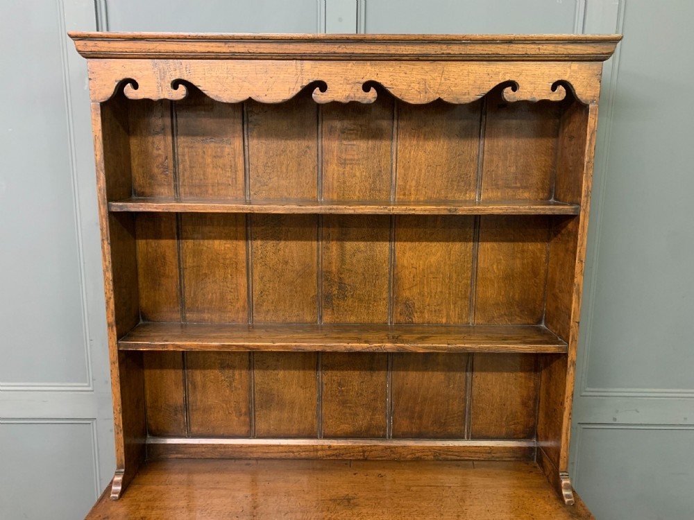 A carved oak Welsh dresser featuring an upper open shelving rack above two carved drawers and panelled cupboard doors resting on turned legs. View X