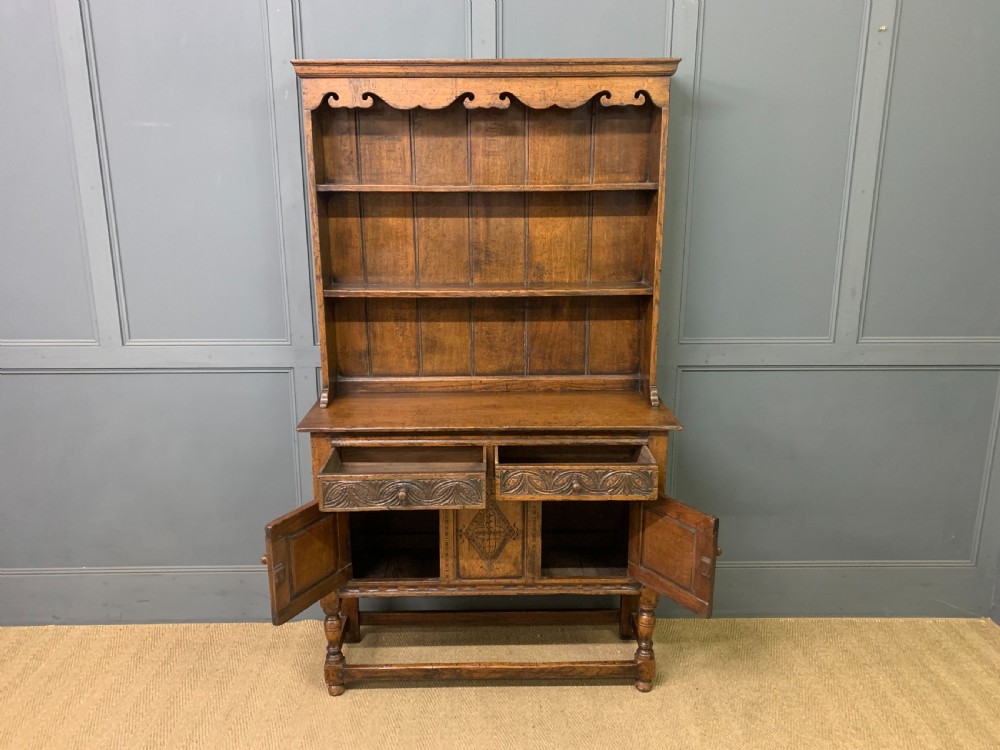 A carved oak Welsh dresser featuring an upper open shelving rack above two carved drawers and panelled cupboard doors resting on turned legs. View XI