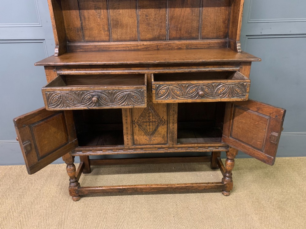 A carved oak Welsh dresser featuring an upper open shelving rack above two carved drawers and panelled cupboard doors resting on turned legs. View XII