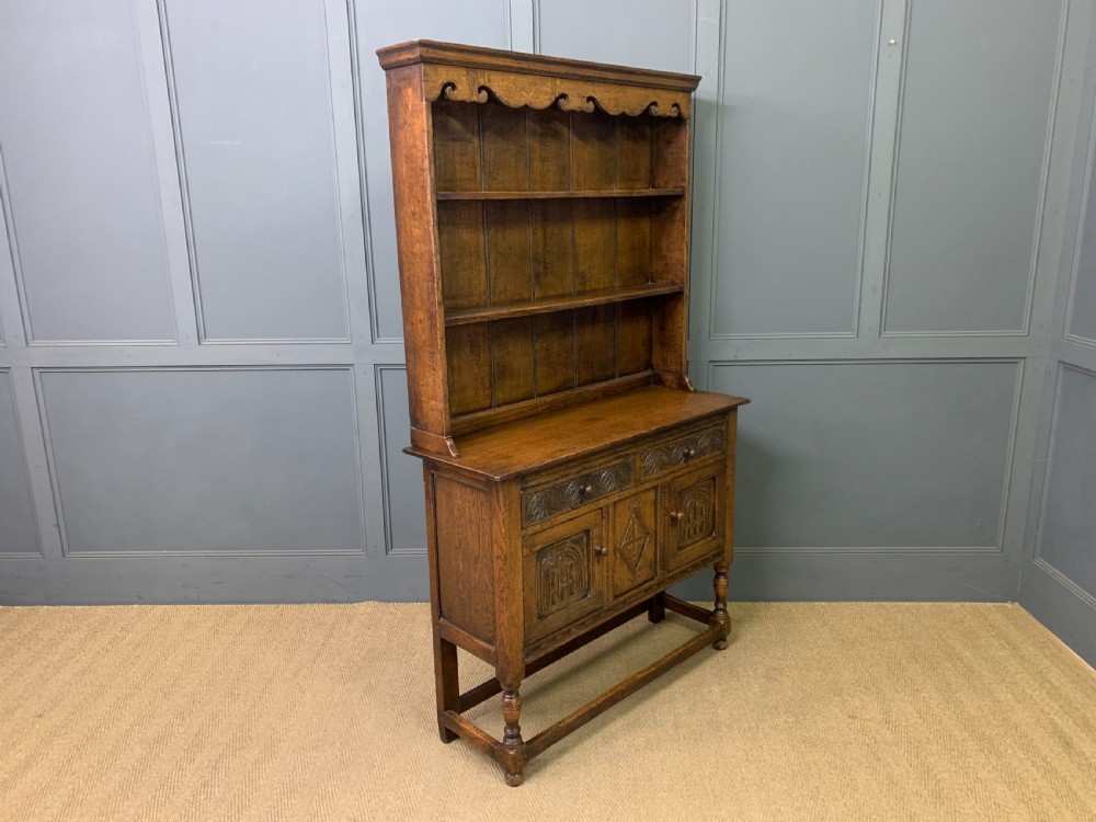 A carved oak Welsh dresser featuring an upper open shelving rack above two carved drawers and panelled cupboard doors resting on turned legs. View XIII