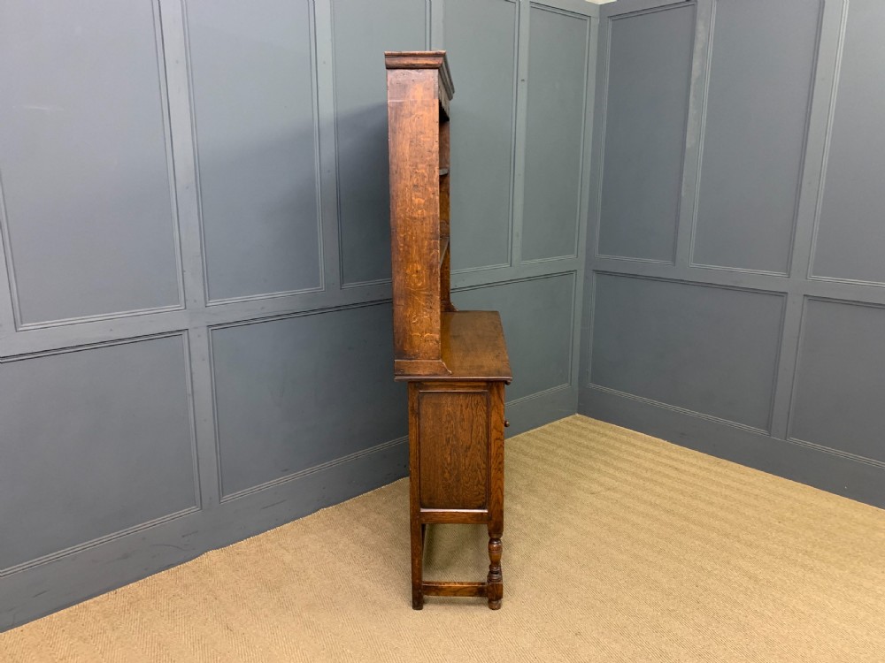 A carved oak Welsh dresser featuring an upper open shelving rack above two carved drawers and panelled cupboard doors resting on turned legs. View XIV