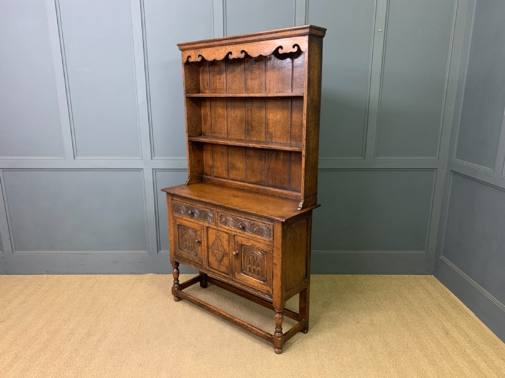 A carved oak Welsh dresser featuring an upper open shelving rack above two carved drawers and panelled cupboard doors resting on turned legs. View XVII