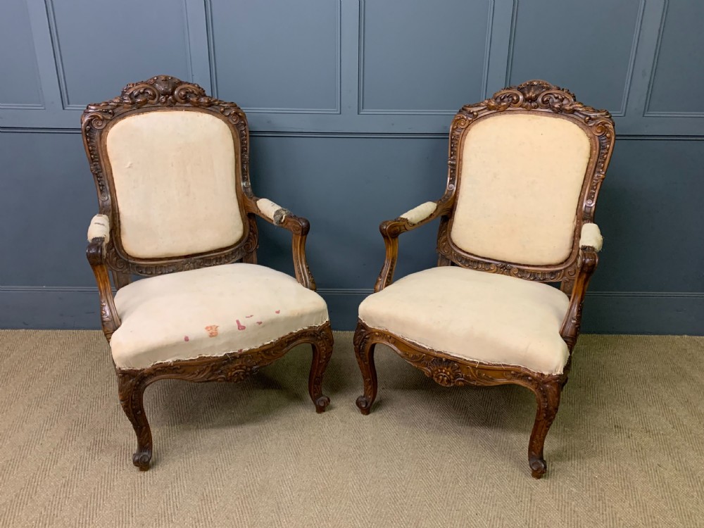 A pair of antique carved walnut French fauteuil armchairs featuring cream fabric upholstery and cabriole legs.