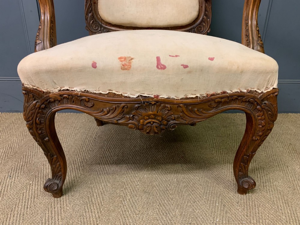 A pair of antique carved walnut French fauteuil armchairs featuring cream fabric upholstery and cabriole legs. View X