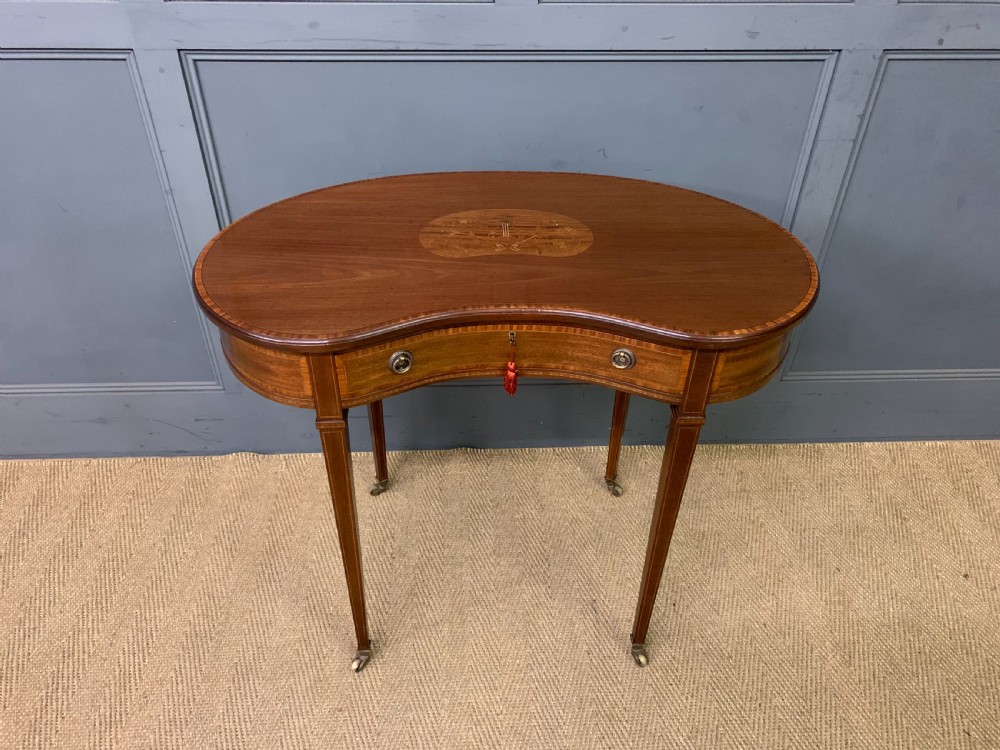 An Edwardian kidney-shaped mahogany table with central marquetry inlay, a single drawer with brass handles, and four tapered legs on castors. View II