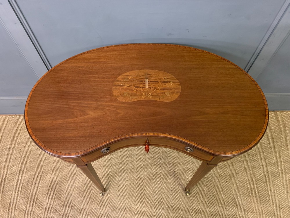 An Edwardian kidney-shaped mahogany table with central marquetry inlay, a single drawer with brass handles, and four tapered legs on castors. View III