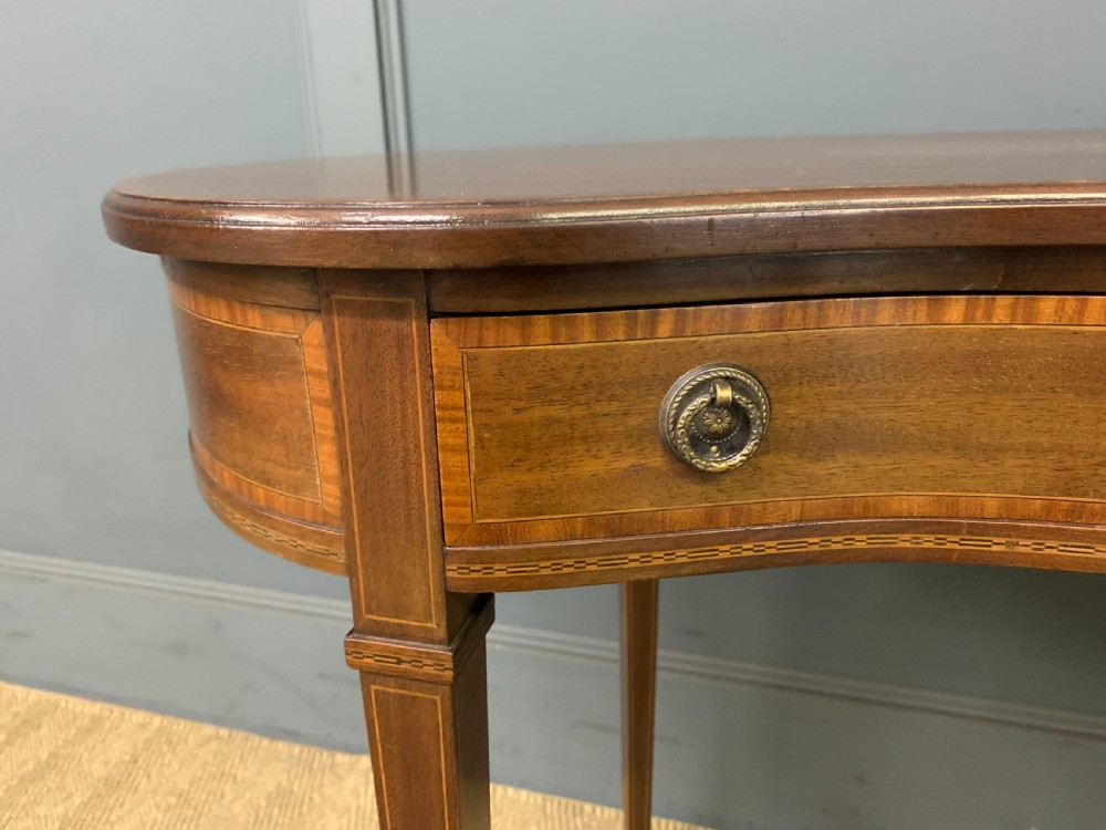 An Edwardian kidney-shaped mahogany table with central marquetry inlay, a single drawer with brass handles, and four tapered legs on castors. View VI