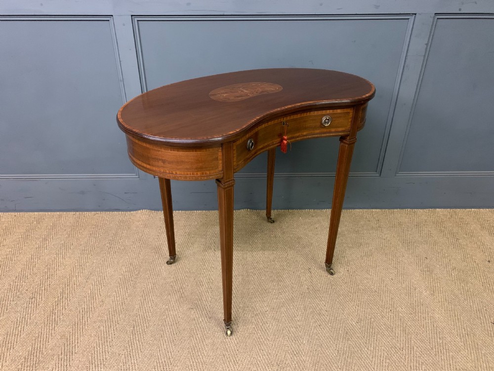 An Edwardian kidney-shaped mahogany table with central marquetry inlay, a single drawer with brass handles, and four tapered legs on castors. View VIII