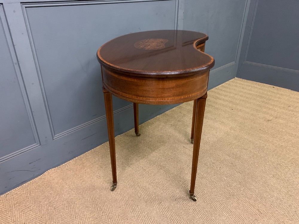 An Edwardian kidney-shaped mahogany table with central marquetry inlay, a single drawer with brass handles, and four tapered legs on castors. View IX
