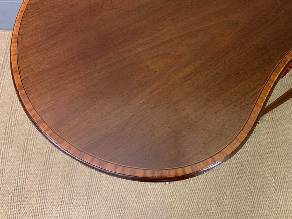 An Edwardian kidney-shaped mahogany table with central marquetry inlay, a single drawer with brass handles, and four tapered legs on castors. View X