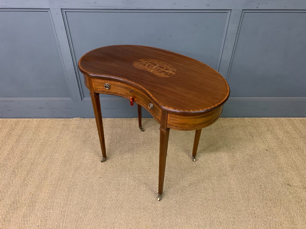 An Edwardian kidney-shaped mahogany table with central marquetry inlay, a single drawer with brass handles, and four tapered legs on castors. View XIII