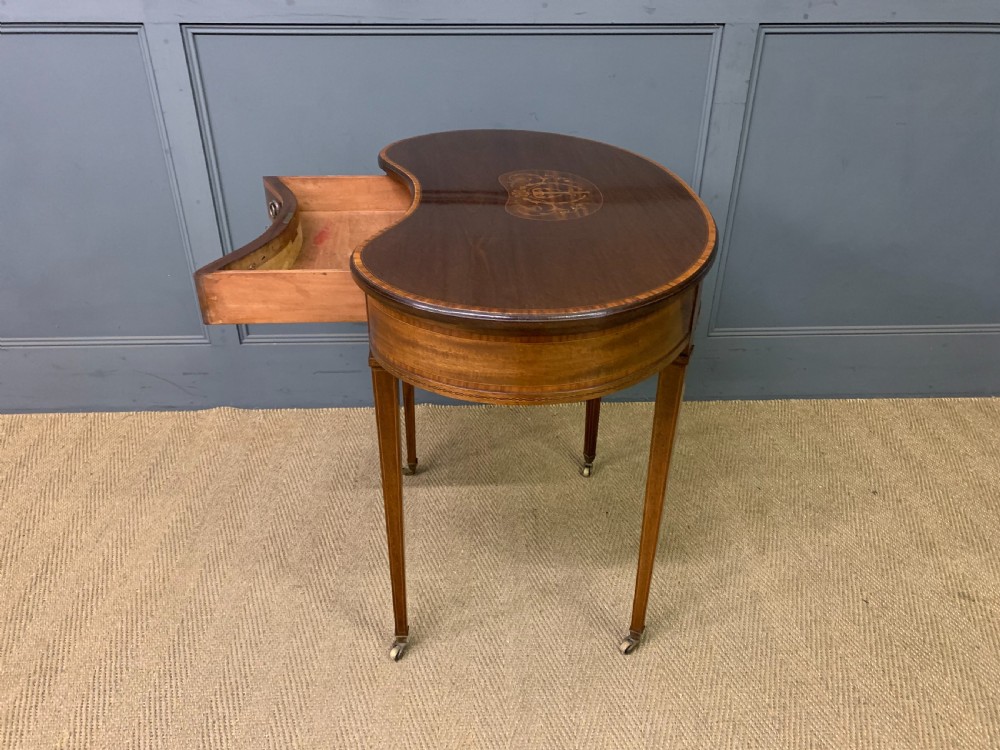An Edwardian kidney-shaped mahogany table with central marquetry inlay, a single drawer with brass handles, and four tapered legs on castors. View XIV