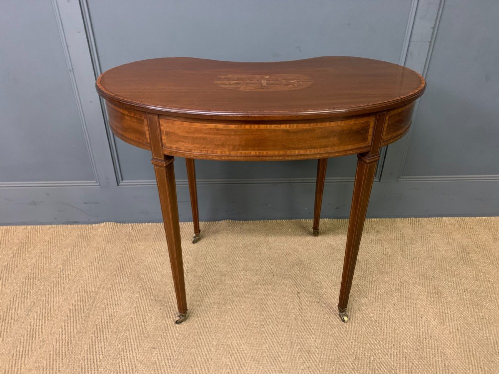 An Edwardian kidney-shaped mahogany table with central marquetry inlay, a single drawer with brass handles, and four tapered legs on castors. View XV