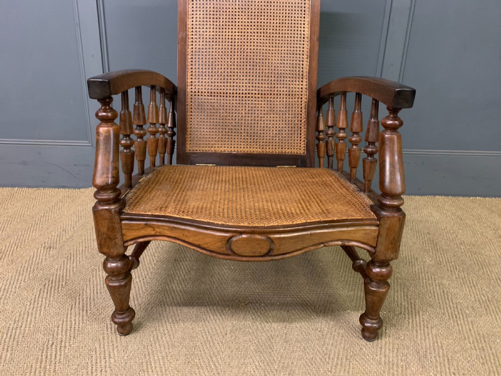 A 19th-century colonial reclining armchair crafted from dark wood with a hand-woven cane backrest and seat, featuring turned spindle arm supports. View III
