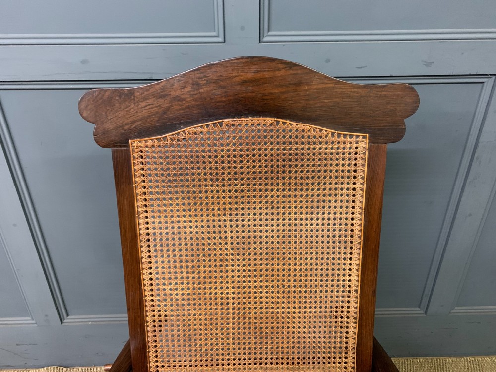 A 19th-century colonial reclining armchair crafted from dark wood with a hand-woven cane backrest and seat, featuring turned spindle arm supports. View IV