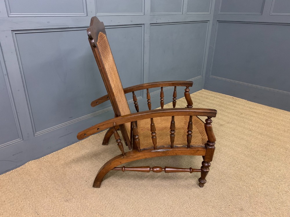 A 19th-century colonial reclining armchair crafted from dark wood with a hand-woven cane backrest and seat, featuring turned spindle arm supports. View VII