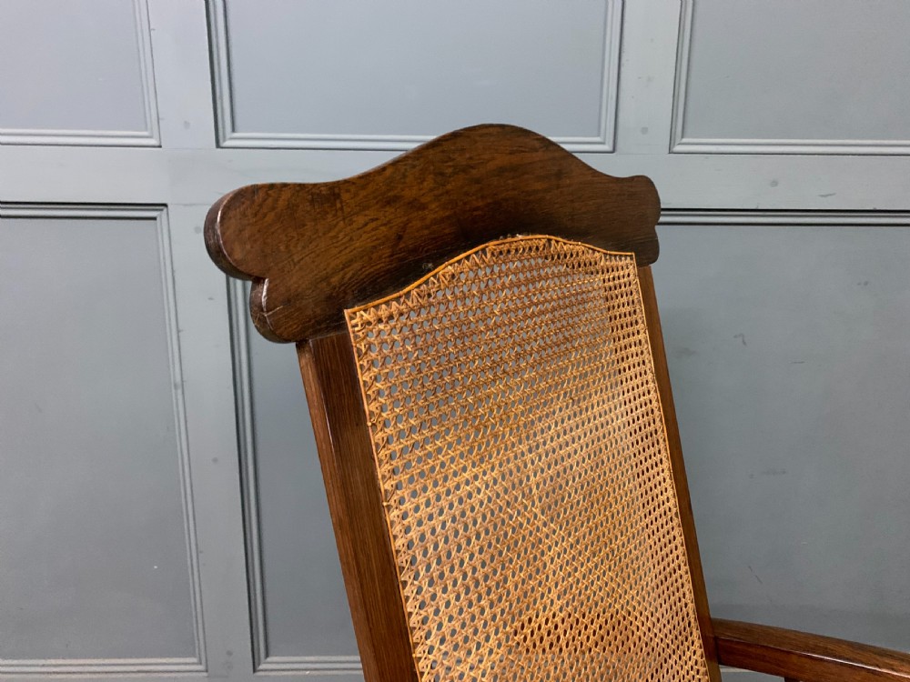 A 19th-century colonial reclining armchair crafted from dark wood with a hand-woven cane backrest and seat, featuring turned spindle arm supports. View VIII