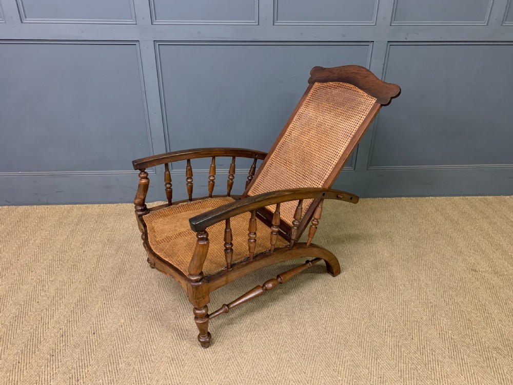 A 19th-century colonial reclining armchair crafted from dark wood with a hand-woven cane backrest and seat, featuring turned spindle arm supports. View XI