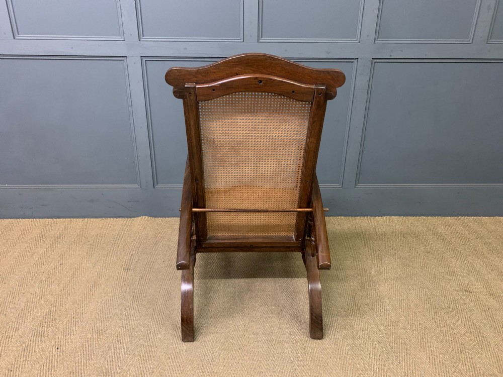 A 19th-century colonial reclining armchair crafted from dark wood with a hand-woven cane backrest and seat, featuring turned spindle arm supports. View XIV