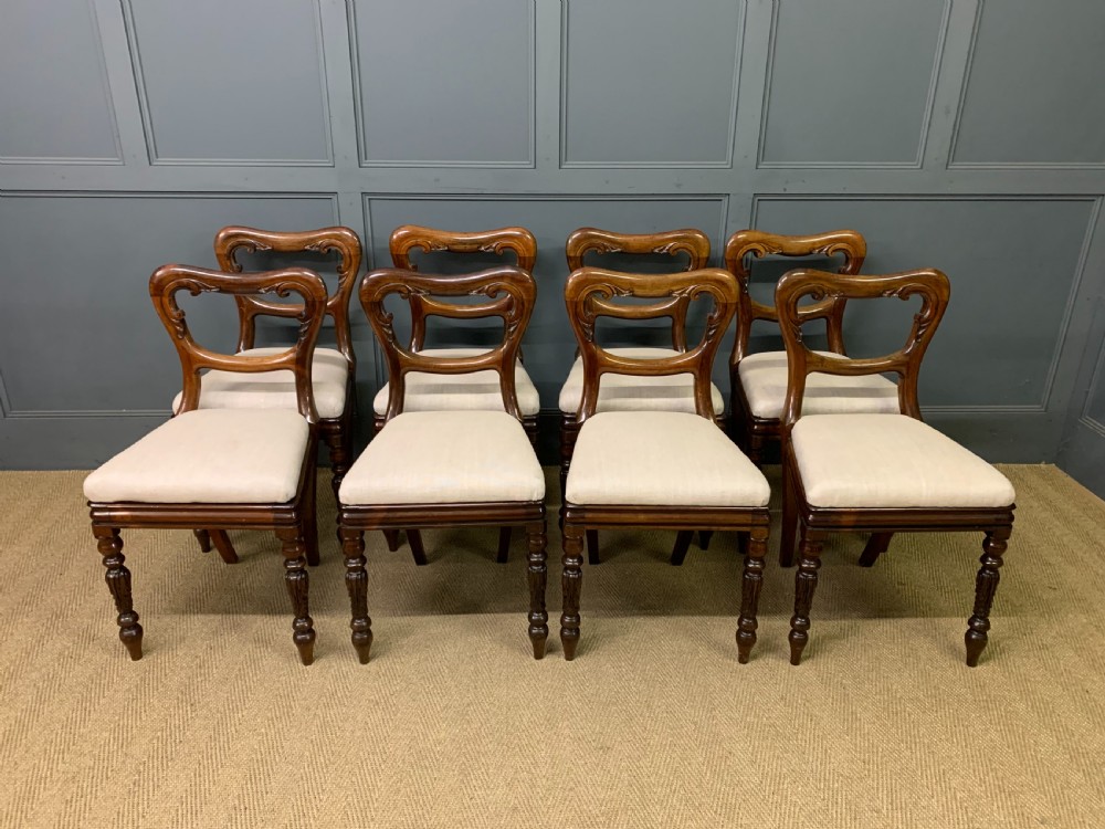 A set of eight early Victorian rosewood dining chairs featuring rounded balloon back frames, carved rail detailing, turned legs, and neutral upholstered seats. View II
