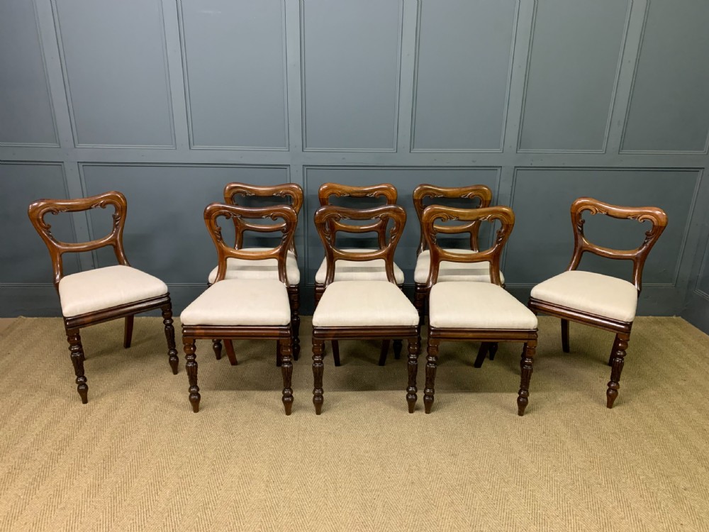 A set of eight early Victorian rosewood dining chairs featuring rounded balloon back frames, carved rail detailing, turned legs, and neutral upholstered seats. View III
