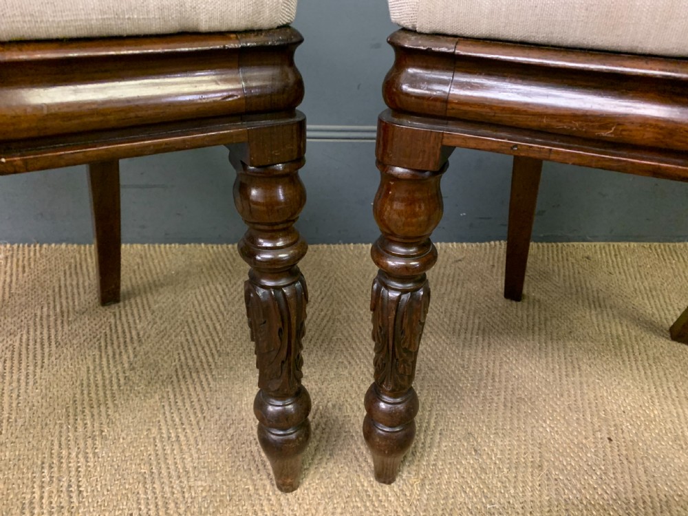 A set of eight early Victorian rosewood dining chairs featuring rounded balloon back frames, carved rail detailing, turned legs, and neutral upholstered seats. View V