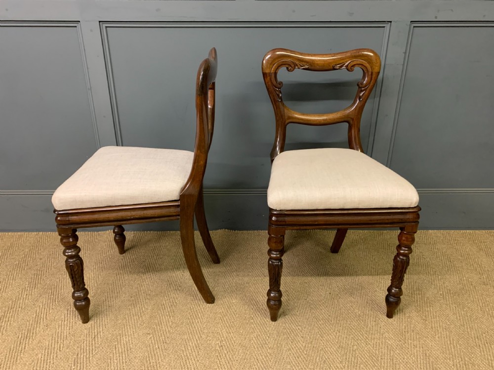 A set of eight early Victorian rosewood dining chairs featuring rounded balloon back frames, carved rail detailing, turned legs, and neutral upholstered seats. View VI