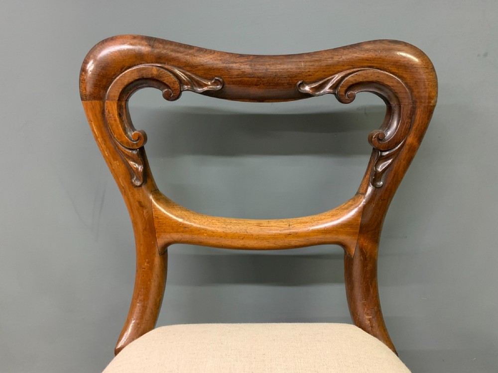A set of eight early Victorian rosewood dining chairs featuring rounded balloon back frames, carved rail detailing, turned legs, and neutral upholstered seats. View X