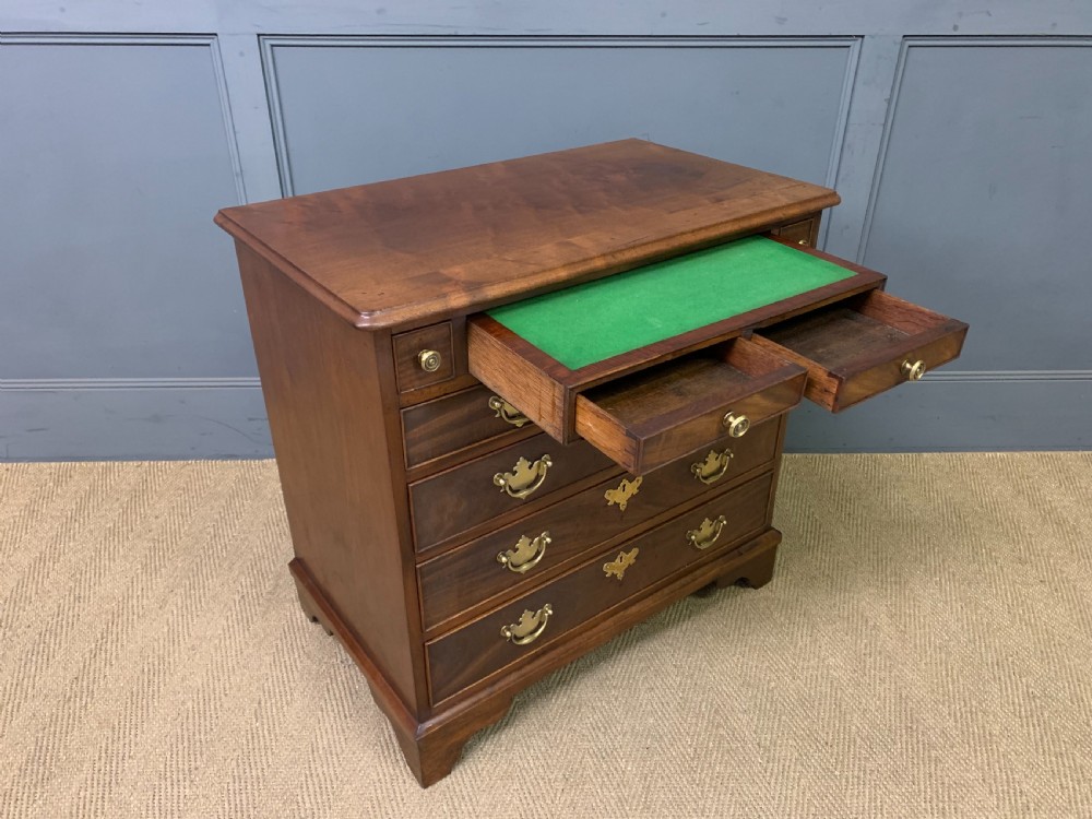 A Georgian mahogany bachelor chest featuring multiple drawers, brass handles, bracket feet, and an extended writing slide lined with green baize.