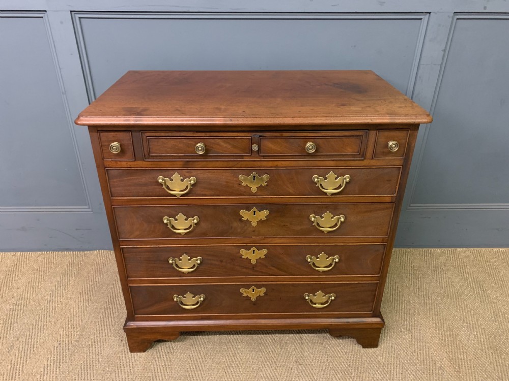 A Georgian mahogany bachelor chest featuring multiple drawers, brass handles, bracket feet, and an extended writing slide lined with green baize. View II
