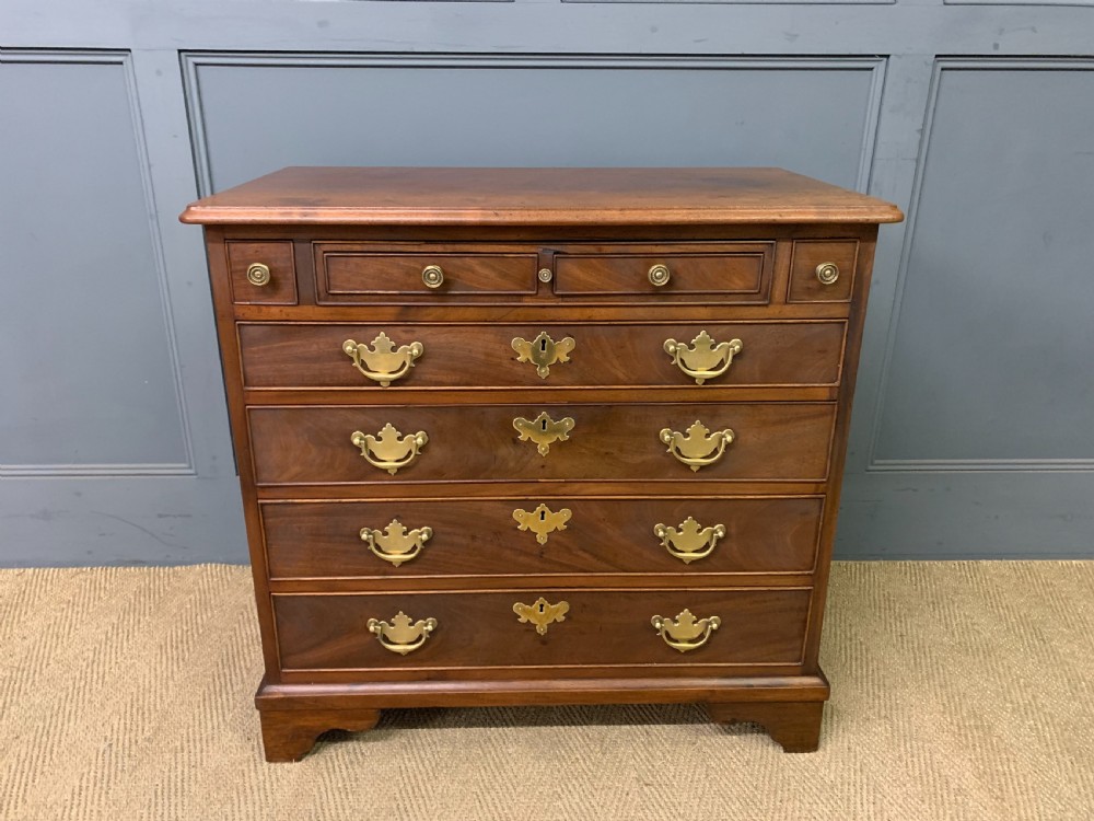 A Georgian mahogany bachelor chest featuring multiple drawers, brass handles, bracket feet, and an extended writing slide lined with green baize. View III